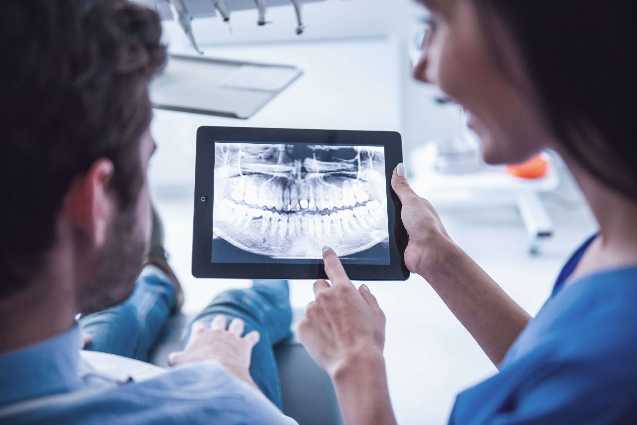 patient and female dentist are looking at teeth image on a digital tablet