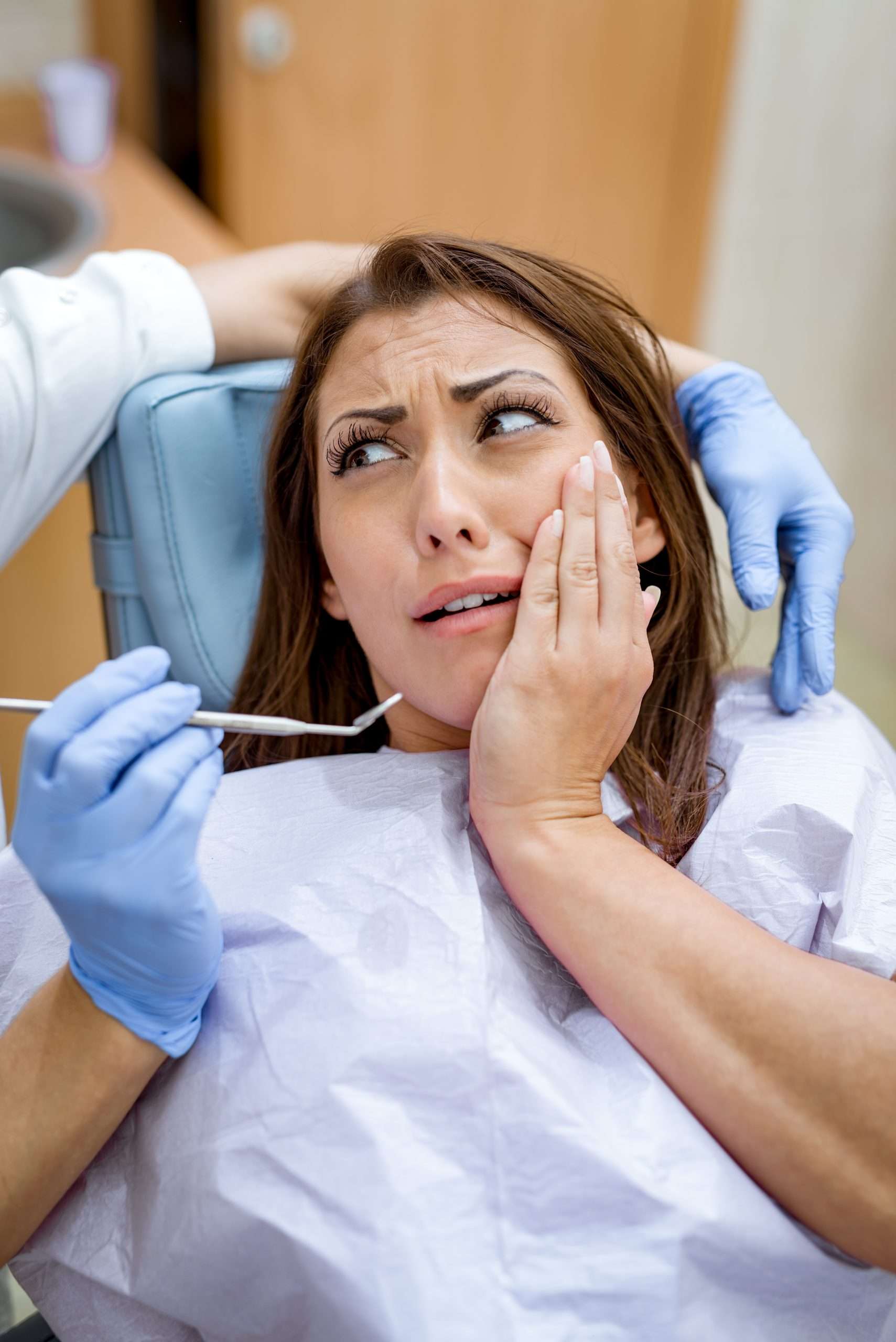 Beautiful young woman in visit at the dentist office with toothache, holding hand over mouth in fear.